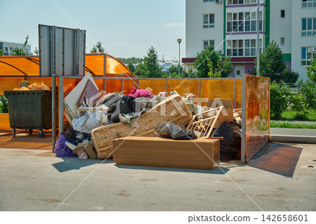 Ground-level view of mixed trash, broken plastic items, and unsorted rubbish scattered around overloaded garbage cans in an apartment courtyard Ground-level view of mixed trash, broken plastic items, and unsorted rubbish scattered around overloaded garbage cans in an apartment courtyard 142658601