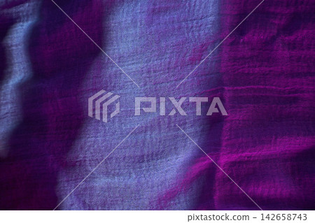 A piece of fabric lies on a surface as light catches its texture. The colors blend from purple to blue A piece of fabric lies on a surface as light catches its texture. The colors blend from purple to blue 142658743