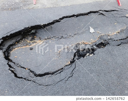 Close up high angle shot of a large dangerous pothole and cracked collapsed asphalt on a city street pavement Close up high angle shot of a large dangerous pothole and cracked collapsed asphalt on a city street pavement 142658762