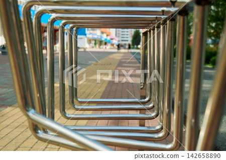 Conceptual through-the-frame framing shot using repeating square stainless steel bike parking racks with a blurred city sidewalk street in the background Conceptual through-the-frame framing shot using repeating square stainless steel bike parking racks with a blurred city sidewalk street in the background 142658890