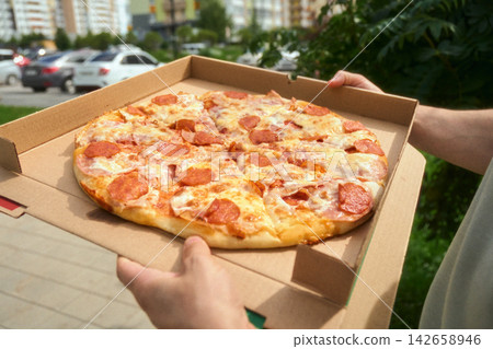 Close up of hands holding fresh pepperoni pizza delivered for modern outdoor picnic Close up of hands holding fresh pepperoni pizza delivered for modern outdoor picnic 142658946