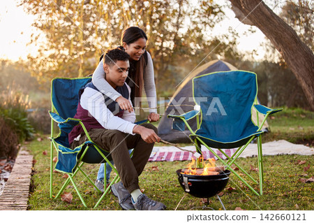 Fire, camping and couple with marshmallows in nature for romantic vacation, adventure or holiday. Love, happy and young man and woman roasting candy by flame on outdoor weekend trip together. Fire, camping and couple with marshmallows in nature for romantic vacation, adventure or holiday. Love, happy and young man and woman roasting candy by flame on outdoor weekend trip together. 142660121