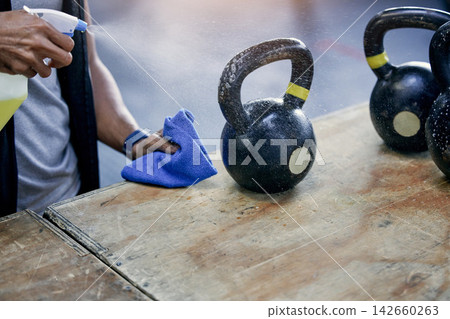 Man, cleaning and gym kettlebell with detergent for hygiene, health and wellness from bacteria. Cleaner, employee and hand to disinfect or sanitise with product for protection or safety from virus Man, cleaning and gym kettlebell with detergent for hygiene, health and wellness from bacteria. Cleaner, employee and hand to disinfect or sanitise with product for protection or safety from virus 142660263