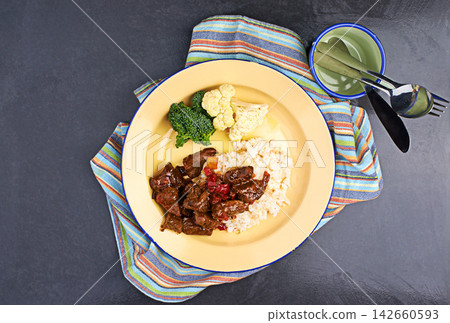 Beef, rice and vegetables for cooking on dark background with broccoli, cutlery and comfort food. Meat stew, starch and cauliflower in kitchen for healthy eating, green color and dinner ingredients Beef, rice and vegetables for cooking on dark background with broccoli, cutlery and comfort food. Meat stew, starch and cauliflower in kitchen for healthy eating, green color and dinner ingredients 142660593