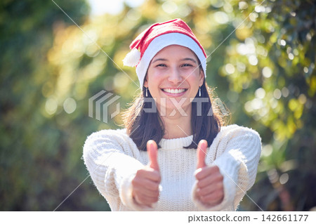 Woman, thumbs up and happy for Christmas in portrait with Santa hat for festive celebration in garden. Girl, person and smile with sign, symbol and icon for yes, like or agreement for xmas cheers Woman, thumbs up and happy for Christmas in portrait with Santa hat for festive celebration in garden. Girl, person and smile with sign, symbol and icon for yes, like or agreement for xmas cheers 142661177