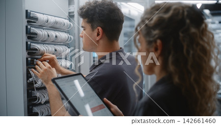 Female IT Engineer Supervising Ethernet Patching with Live Server Telemetry Female IT Engineer Supervising Ethernet Patching with Live Server Telemetry 142661460