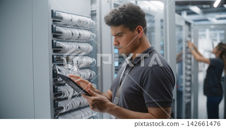 Male Data Center Engineer Inspecting Rack Connections While Using Tablet Male Data Center Engineer Inspecting Rack Connections While Using Tablet 142661476