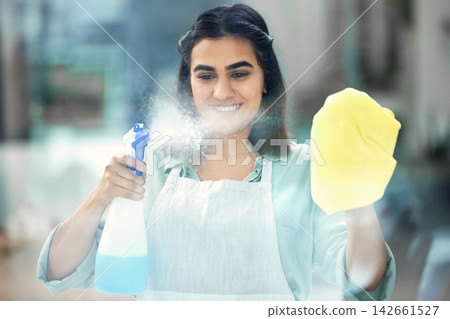Woman, spray and smile with gloves on cloth in house for cleaning, scrub and dirt on window. Housekeeper, happy and apron with textile or detergent in bottle for dust in home by living room. Woman, spray and smile with gloves on cloth in house for cleaning, scrub and dirt on window. Housekeeper, happy and apron with textile or detergent in bottle for dust in home by living room. 142661527
