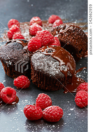 Berry, cupcake and fruit by dark background for chocolate, liquid and dessert with icing sugar. Raspberry, muffin and white powder on countertop with red color for bakery, rich taste and sweet food Berry, cupcake and fruit by dark background for chocolate, liquid and dessert with icing sugar. Raspberry, muffin and white powder on countertop with red color for bakery, rich taste and sweet food 142662959