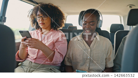 Phone, music and friends in car for road trip, travel or journey together on summer vacation. Smile, social media and headphones with young women on mobile app in vehicle for holiday transportation Phone, music and friends in car for road trip, travel or journey together on summer vacation. Smile, social media and headphones with young women on mobile app in vehicle for holiday transportation 142663532