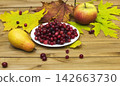 Autumn Still Life. Cranberries on a white plate, autumn leaves and an apple with a pear 142663730