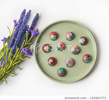 Collectible handmade tempered chocolate sweets with a glossy painted body on a round plate with blur elements. View from above 142663731