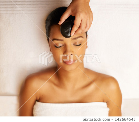 Woman, relax and spa with hot rock for facial treatment, zen or stress relief above at resort. Top view of calm female person with stone on face for beauty, wellness or therapy in relaxation at salon Woman, relax and spa with hot rock for facial treatment, zen or stress relief above at resort. Top view of calm female person with stone on face for beauty, wellness or therapy in relaxation at salon 142664545