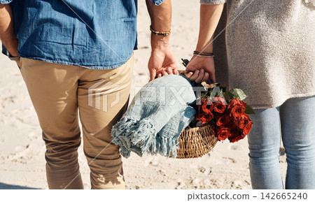 Couple, beach and picnic basket with flowers in walking, back and holiday for vacation, ocean and cropped shot. Romantic, summer and red roses, bonding and sea or outdoor, sand and romance in love 142665240