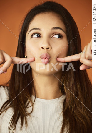 Funny face, fingers and woman in studio for humor, comedy or cheeks dimples on orange background. Female person, lips and playful gen z model for comic emoji, silly facial expression or joking mood 142665326