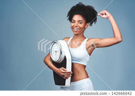 Black girl, portrait and bicep for scale in studio, weight loss and confident measure on blue background. Female person, fitness and diet for balance, mockup space and strong proud for empowerment 142666842