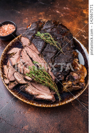 Baked and sliced Venison leg. roast meat of deer with bone on a plate. brown background. top view Baked and sliced Venison leg. roast meat of deer with bone on a plate. brown background. top view 142667571