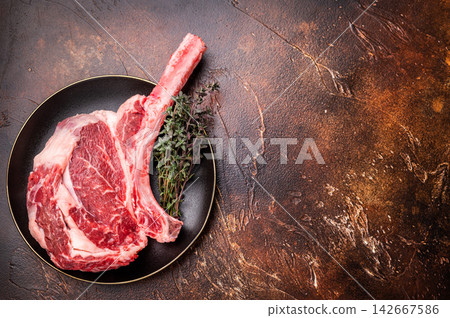 Fresh Tomahawk beef steak, raw marbled rib eye with bone on plate with herbs. brown background. top view Fresh Tomahawk beef steak, raw marbled rib eye with bone on plate with herbs. brown background. top view 142667586