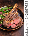 Grilled and sliced Tomahawk beef steak, marble rib eye with bone on plate with salad. brown background. top view 142667623