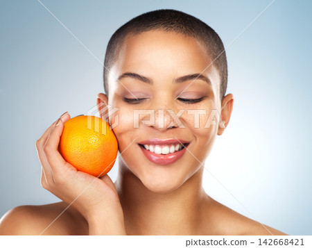 Skincare, beauty and woman with orange in studio for natural, organic and facial treatment. Wellness, health and model with citrus fruit with vitamin c for face dermatology routine by gray background Skincare, beauty and woman with orange in studio for natural, organic and facial treatment. Wellness, health and model with citrus fruit with vitamin c for face dermatology routine by gray background 142668421