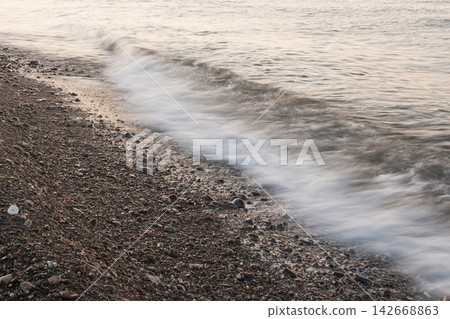 Long exposure sea wave motion line rushing along pebble shore at sunset Long exposure sea wave motion line rushing along pebble shore at sunset 142668863
