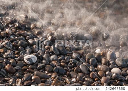 Long exposure close up of sea wave motion over smooth wet pebbles 142668868