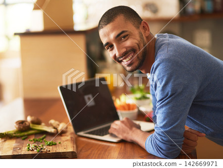 Man, portrait and vegetables on table with laptop for recipe research, ingredients list or dinner ideas on website. Tech, male person or nutritionist online for healthy diet and wellness in home 142669971