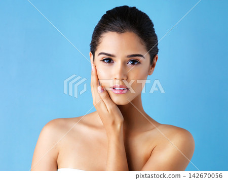 Touch, skincare and portrait of woman in studio with natural beauty, confidence and luxury cosmetics. Dermatology, facial care and girl with shine, wellness and healthy skin glow on blue background. Touch, skincare and portrait of woman in studio with natural beauty, confidence and luxury cosmetics. Dermatology, facial care and girl with shine, wellness and healthy skin glow on blue background. 142670056