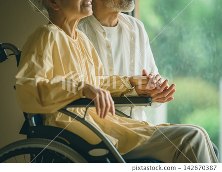一名男子輕輕握住坐在輪椅上的老婦人的手,安慰她。 一名男子輕輕握住坐在輪椅上的老婦人的手,安慰她。 142670387
