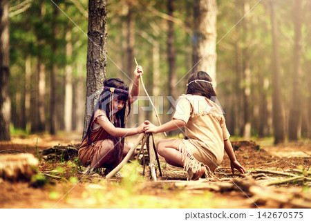 Native American children, girl and outdoor for campfire with helping hand, teaching or learning. Kids, siblings and wood for flame with development of survival skill in forest with branches on ground Native American children, girl and outdoor for campfire with helping hand, teaching or learning. Kids, siblings and wood for flame with development of survival skill in forest with branches on ground 142670575