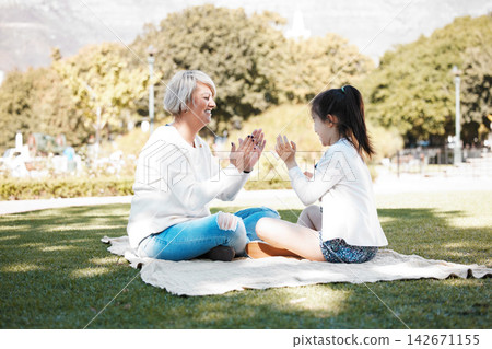Family, game or pattycake with grandmother and child outdoor on grass lawn together for bonding. Love, smile senior woman with girl grandkid at park for picnic, retirement or break in summer Family, game or pattycake with grandmother and child outdoor on grass lawn together for bonding. Love, smile senior woman with girl grandkid at park for picnic, retirement or break in summer 142671155