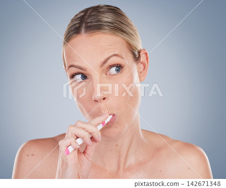 Woman, thinking and brushing teeth in studio ideas for self care and dental wellness on background. Healthy, cleaning model with toothbrush, toothpaste and plan for dentistry, healthcare or routine Woman, thinking and brushing teeth in studio ideas for self care and dental wellness on background. Healthy, cleaning model with toothbrush, toothpaste and plan for dentistry, healthcare or routine 142671348
