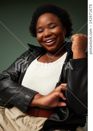Happy, african woman and fashion with leather jacket for plus size aesthetic outfit isolated in studio. Female person, smile and portrait with edgy clothes for pride and style on green background Happy, african woman and fashion with leather jacket for plus size aesthetic outfit isolated in studio. Female person, smile and portrait with edgy clothes for pride and style on green background 142671678