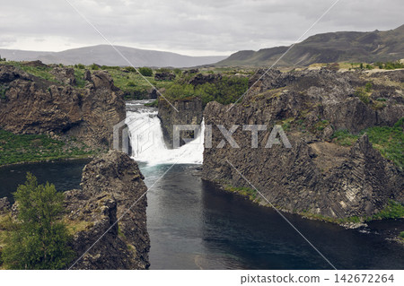 Hjalparfoss waterfall and an expansive patterned basalt wall amid volcanic terrain in Iceland Hjalparfoss waterfall and an expansive patterned basalt wall amid volcanic terrain in Iceland 142672264