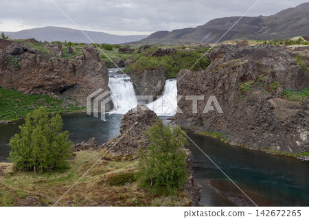 Hjalparfoss waterfall beyond a green volcanic terrain in the Icelandic outdoors Hjalparfoss waterfall beyond a green volcanic terrain in the Icelandic outdoors 142672265