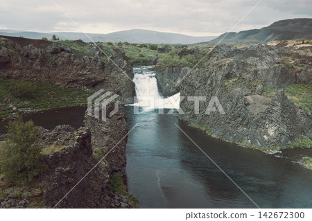 Hjalparfoss waterfall beyond a winding pool and volcanic rocks in Iceland Hjalparfoss waterfall beyond a winding pool and volcanic rocks in Iceland 142672300