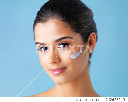 Woman, portrait and face cream or skincare in studio on blue background for dermatology, treatment or hygiene. Female person, lotion and sunscreen protection with healthy cosmetics, facial or beauty Woman, portrait and face cream or skincare in studio on blue background for dermatology, treatment or hygiene. Female person, lotion and sunscreen protection with healthy cosmetics, facial or beauty 142672343