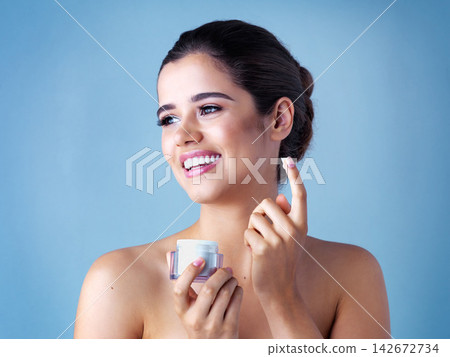 Woman, hand and apply face cream for moisturizing skincare or dermatology, thinking or blue background. Female person, jar and cosmetic beauty for health treatment or wellness, sunscreen or studio Woman, hand and apply face cream for moisturizing skincare or dermatology, thinking or blue background. Female person, jar and cosmetic beauty for health treatment or wellness, sunscreen or studio 142672734