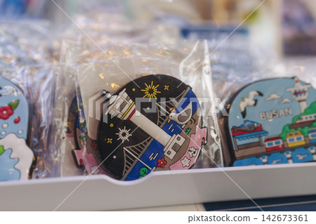 Tourist gifts and Korean souvenirs from Busan, South Korea, toys and figurines, fridge magnets and key ring keychain, key fobs and postcards with symbols of Busan in a local gift vendor shop market Tourist gifts and Korean souvenirs from Busan, South Korea, toys and figurines, fridge magnets and key ring keychain, key fobs and postcards with symbols of Busan in a local gift vendor shop market 142673361