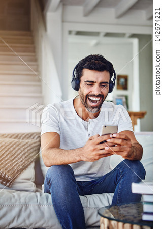 Man, headphones and laughing with phone on sofa for funny video, social media post and comedy movie on mobile app. Person, smartphone and happy for listening to audio, sound and subscription in home Man, headphones and laughing with phone on sofa for funny video, social media post and comedy movie on mobile app. Person, smartphone and happy for listening to audio, sound and subscription in home 142674221