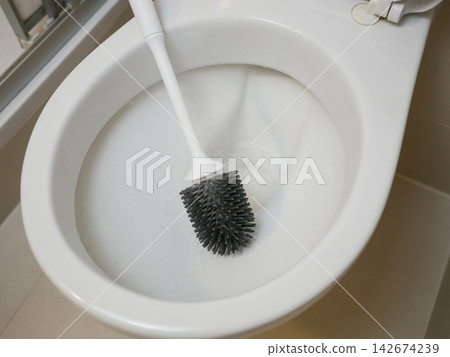 Close-up of white toilet bowl with black silicone brush and foam - cleaning, hygiene and bathroom freshness concept. Close-up of white toilet bowl with black silicone brush and foam - cleaning, hygiene and bathroom freshness concept. 142674239