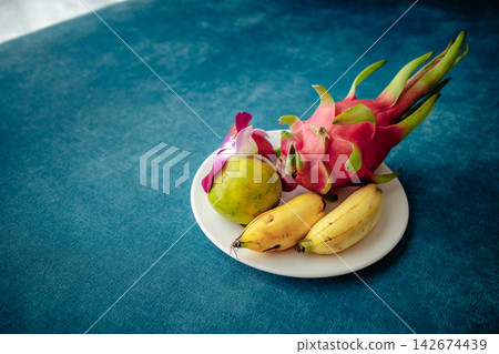 一盤色彩鮮豔的熱帶水果——火龍果、香蕉、青檸和蘭花——盛在白色盤子裡。 一盤色彩鮮豔的熱帶水果——火龍果、香蕉、青檸和蘭花——盛在白色盤子裡。 142674439
