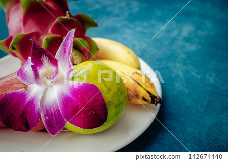 A close-up photograph of a vibrant purple orchid placed on top of green tropical fruit. A close-up photograph of a vibrant purple orchid placed on top of green tropical fruit. 142674440