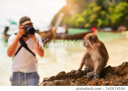 Man, camera and monkey with sunshine, beach and tropical island with getaway trip, Bali and seaside. Person, photographer and tourist with memory, travel and summer with wild animal and adventure 142674584