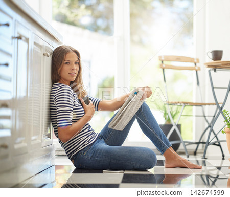 Woman, newspaper and portrait in home on kitchen floor for reading, global headlines or report with coffee. Person, press and print media with information for international news story at apartment 142674599