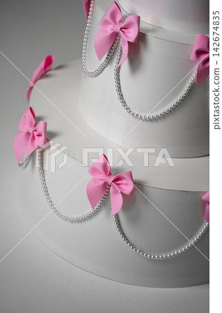 Coquette style wedding cake decor with pink bows and pearl beads on grey background 142674835