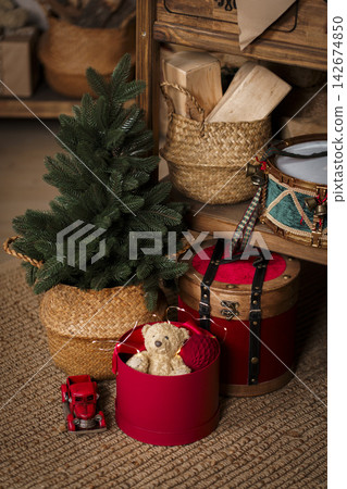 Christmas red gift box with teddy bear and small xmas tree in wicker basket on jute rug background Christmas red gift box with teddy bear and small xmas tree in wicker basket on jute rug background 142674850
