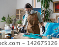 Female artist refining patterns in uncured epoxy resin painting with slender wooden stick at home. 142675126