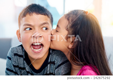 Young, children and annoyed in kiss on cheek with cute in home as kids in youth. Siblings, expression and irritated as brother and sister on couch in affection, love and childhood development Young, children and annoyed in kiss on cheek with cute in home as kids in youth. Siblings, expression and irritated as brother and sister on couch in affection, love and childhood development 142675292