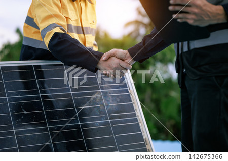 Two workers shake hands beside a solar panel outdoors, a renewable energy partnership, installation agreement, and clean power business deal. Two workers shake hands beside a solar panel outdoors, a renewable energy partnership, installation agreement, and clean power business deal. 142675366